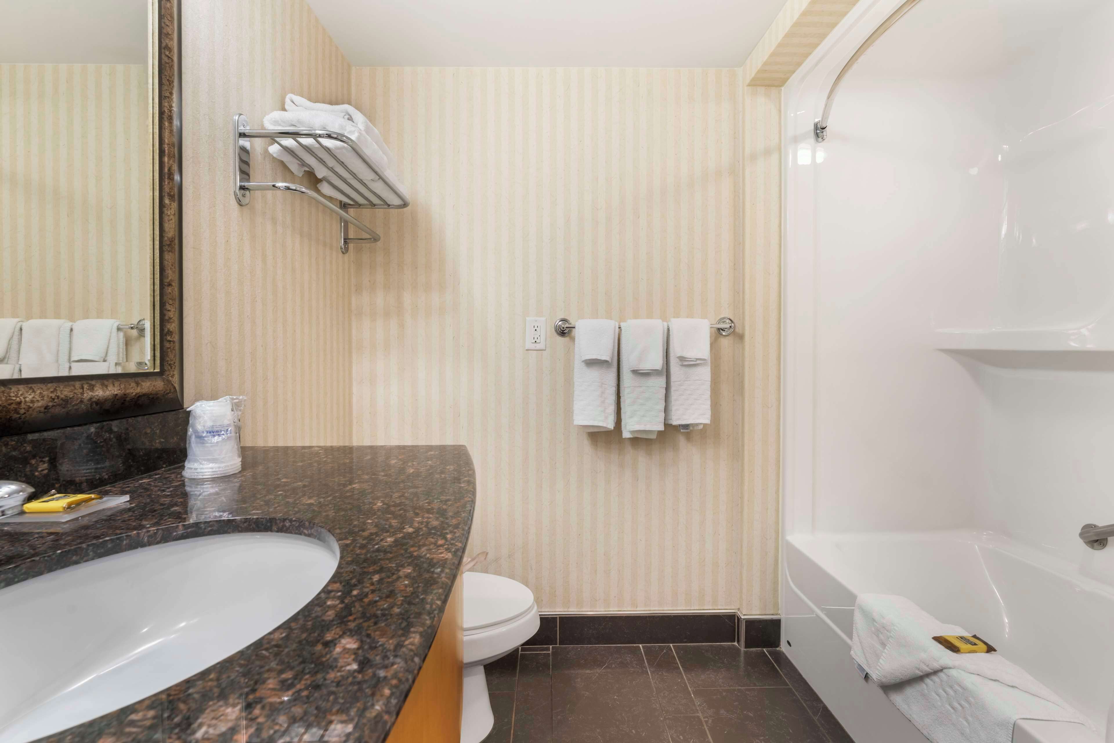 Un baño con lavamanos de encimera de granito, inodoro, toallero con toallas y bañera.
