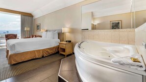 A hotel room with a large bed, a separate bathroom with a bathtub, a small bedside table, a nightstand, and a window with a view.