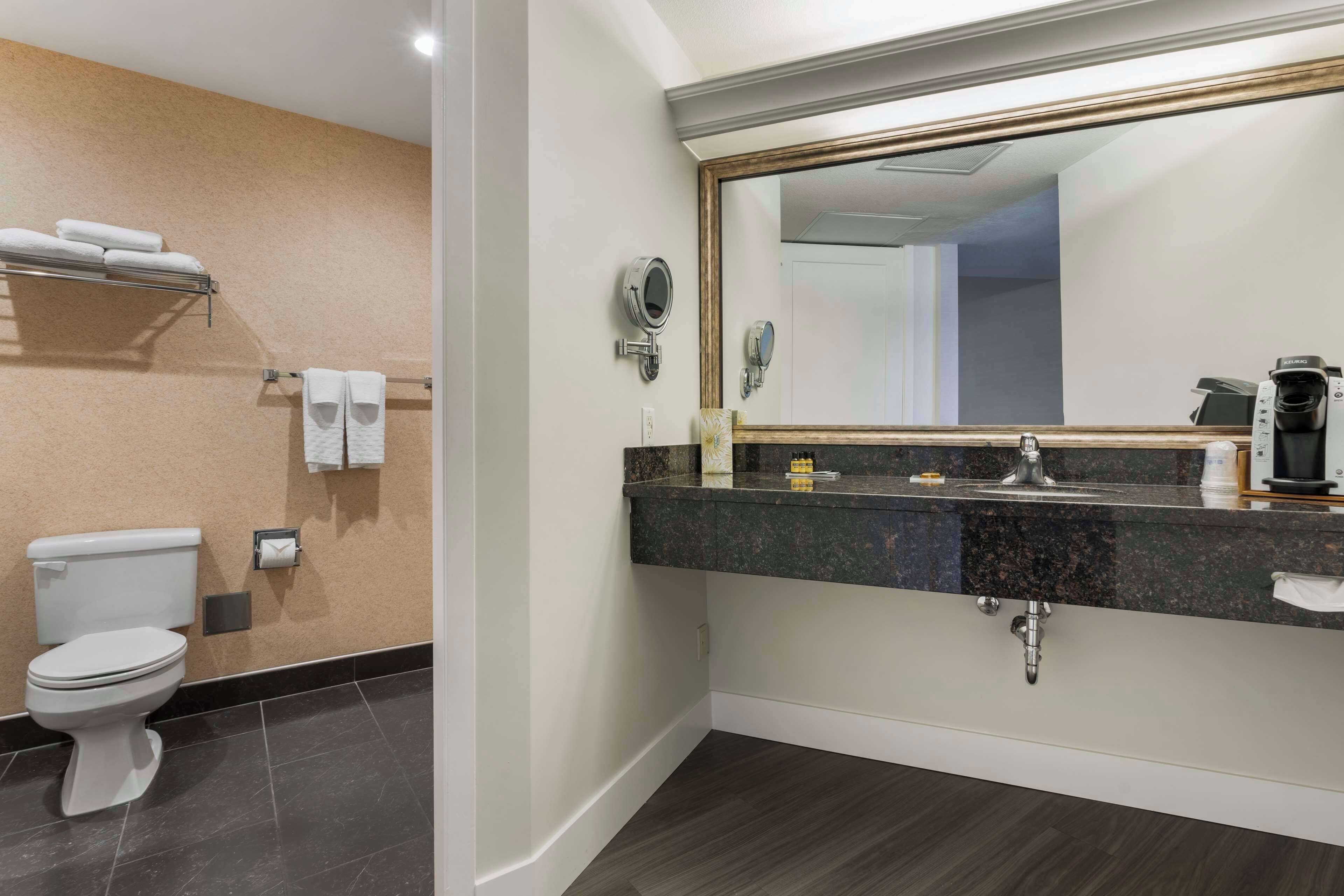 Une salle de bain équipée de toilettes, d’un porte-serviettes, d’un lavabo, d’un miroir et d’une machine à café.