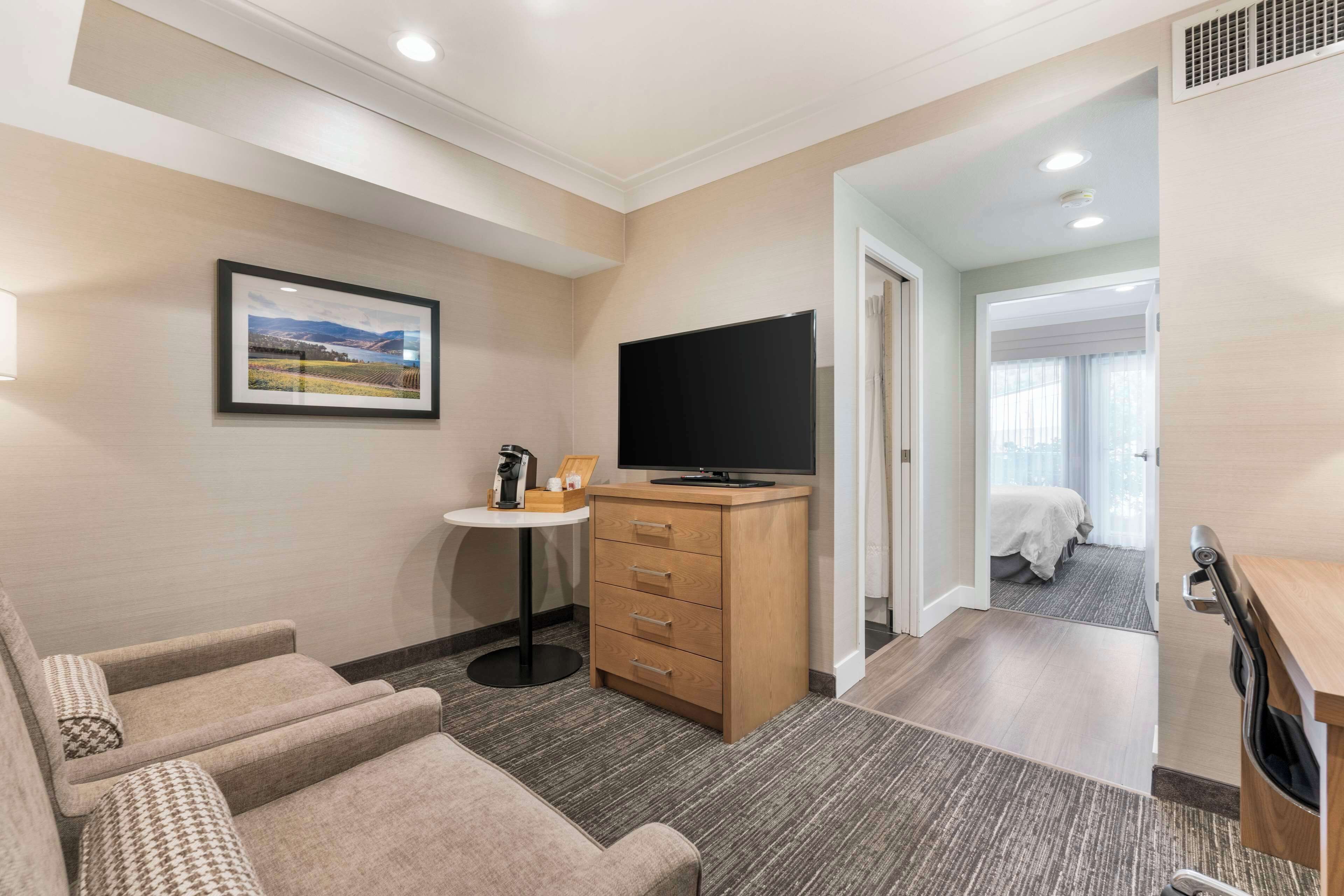 A hotel room with a sofa, a TV, a small table with a coffee maker, and a bed in the adjacent room.