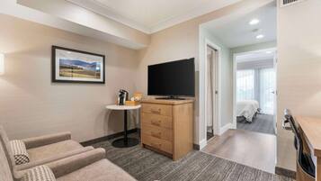 A hotel room with a sofa, a TV, a small table with a coffee maker, and a bed in the adjacent room.