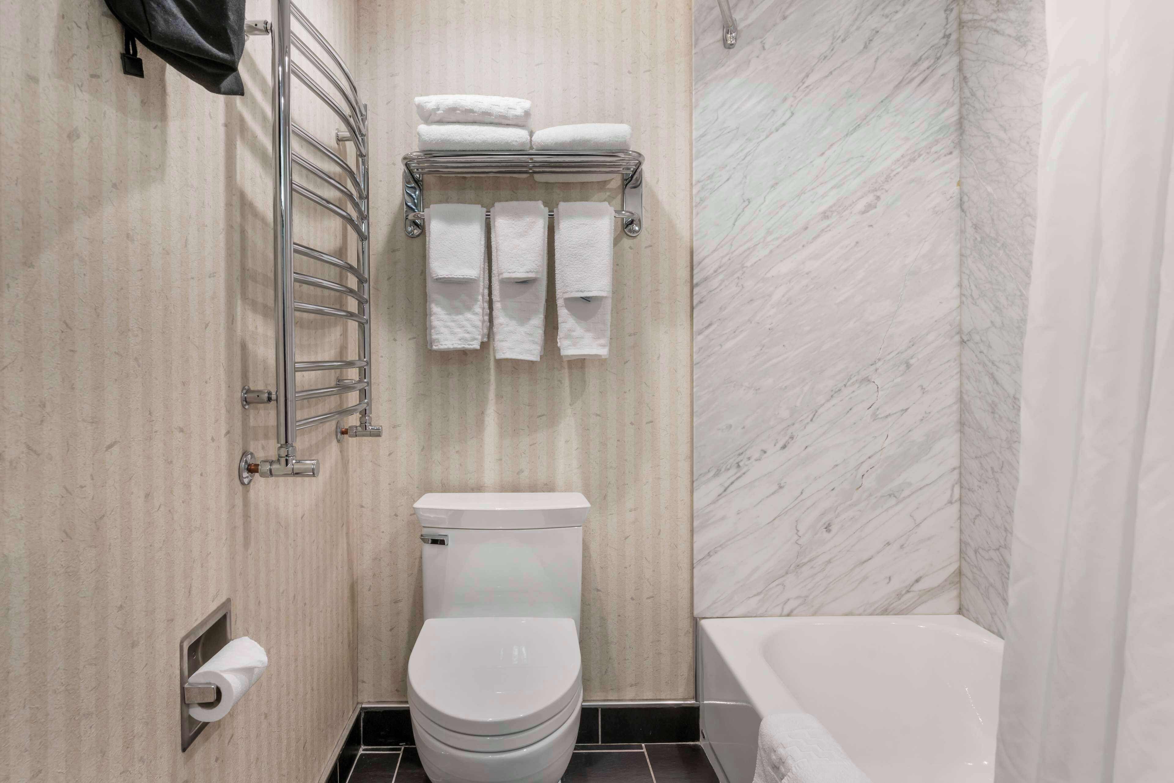 Une salle de bain moderne comprenant des toilettes, un porte-serviettes avec des serviettes pliées et un espace douche.
