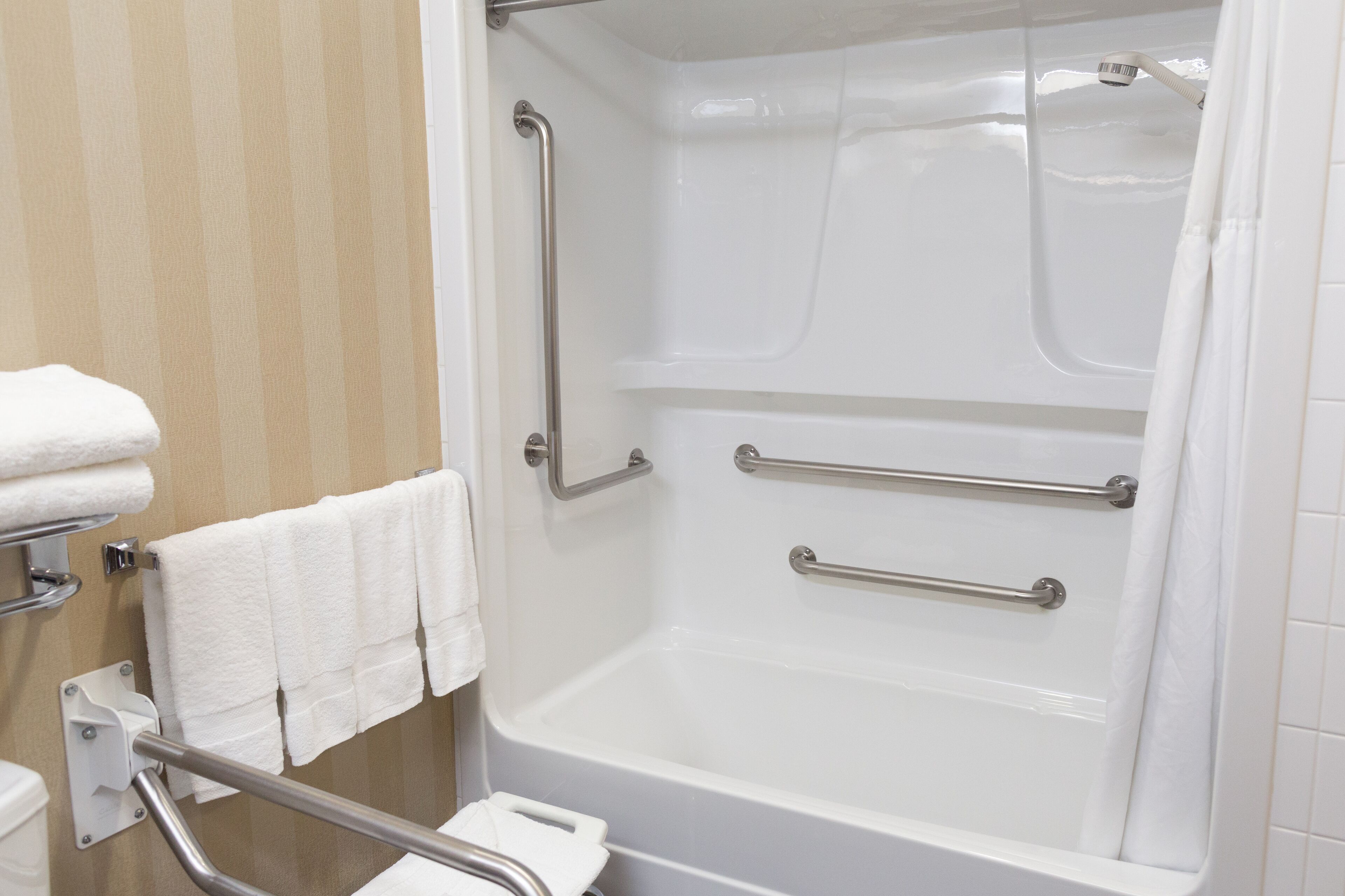 A bathroom with a white bathtub, grab bars, and a towel rack.