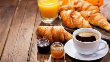 Et træbord med croissanter, et glas appelsinjuice, en kop kaffe og to små dåser marmelade.