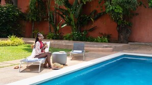 Un área junto a la piscina con una tumbona, una mesita redonda y una persona leyendo un libro.