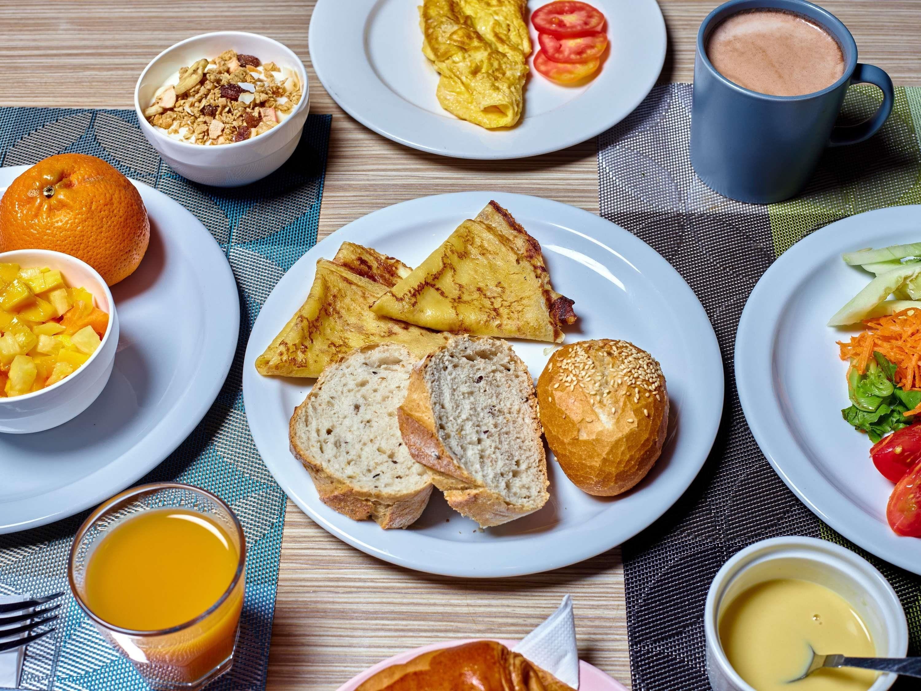 A breakfast setting with plates of toast, bread rolls, and a bowl of fruit.