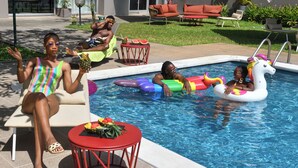 Zona de piscina con sillas de descanso, una mesa roja con frutero y juguetes inflables.
