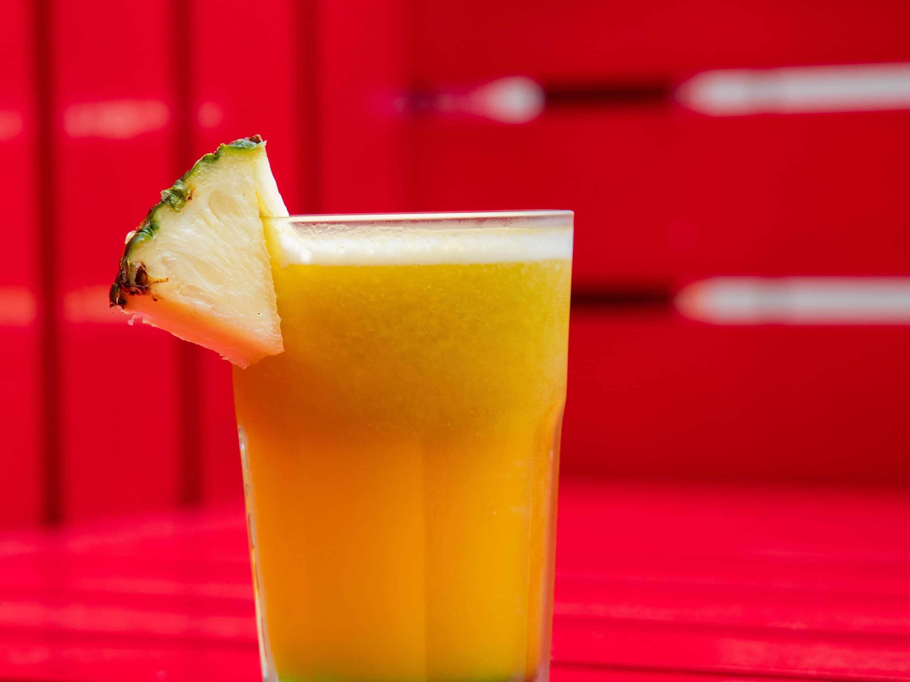 A glass of orange juice with a lime wedge on a red surface.