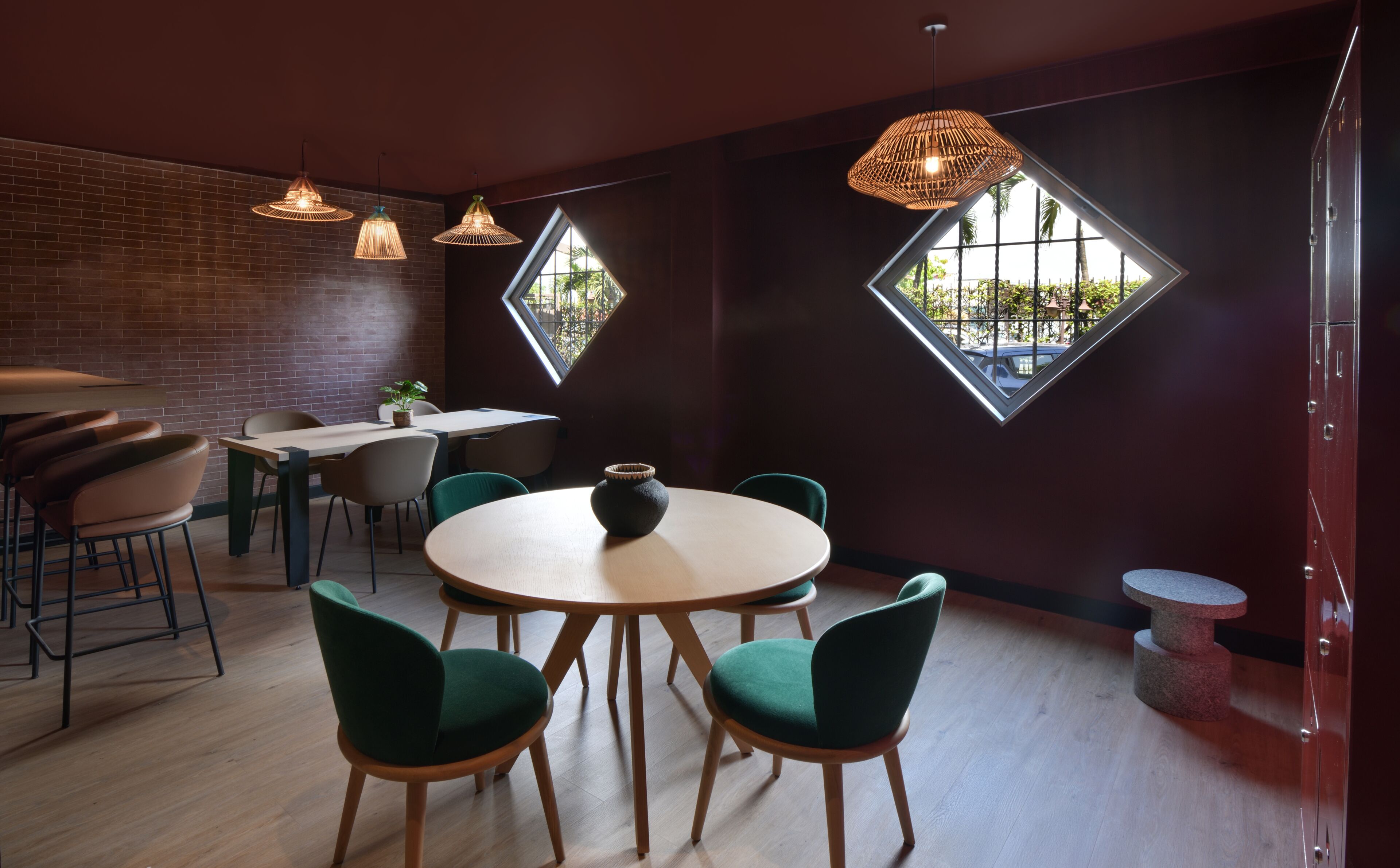 Un espace de restauration moderne avec des tables rondes, des chaises vertes et des luminaires suspendus.