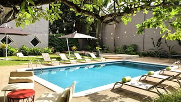 Un área de piscina con sillones de descanso, una pequeña mesa y sombrillas.