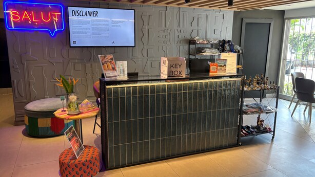 A reception desk with a neon sign, a disclaimer board, a key box, and a display of shoes. - ibis Styles Abidjan Marcory (Abidjan)