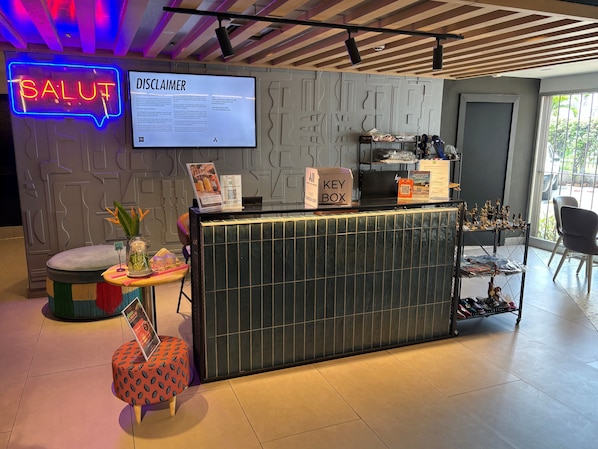 A reception desk with a neon sign, a disclaimer board, a key box, and a display of shoes. - ibis Styles Abidjan Marcory (Abidjan)