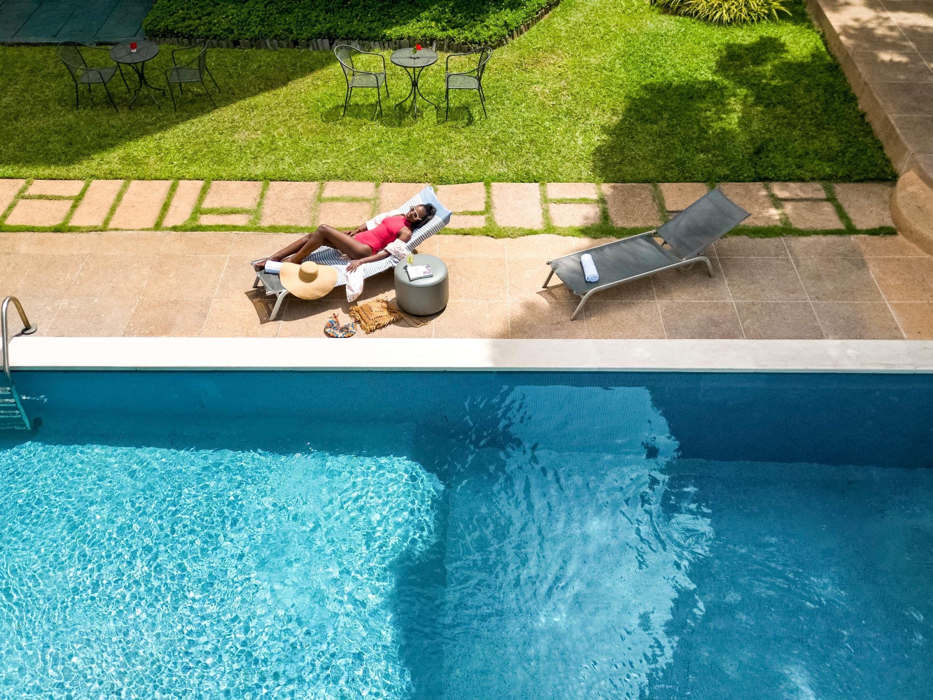 An outdoor swimming pool with lounge chairs and a person relaxing on a chair.