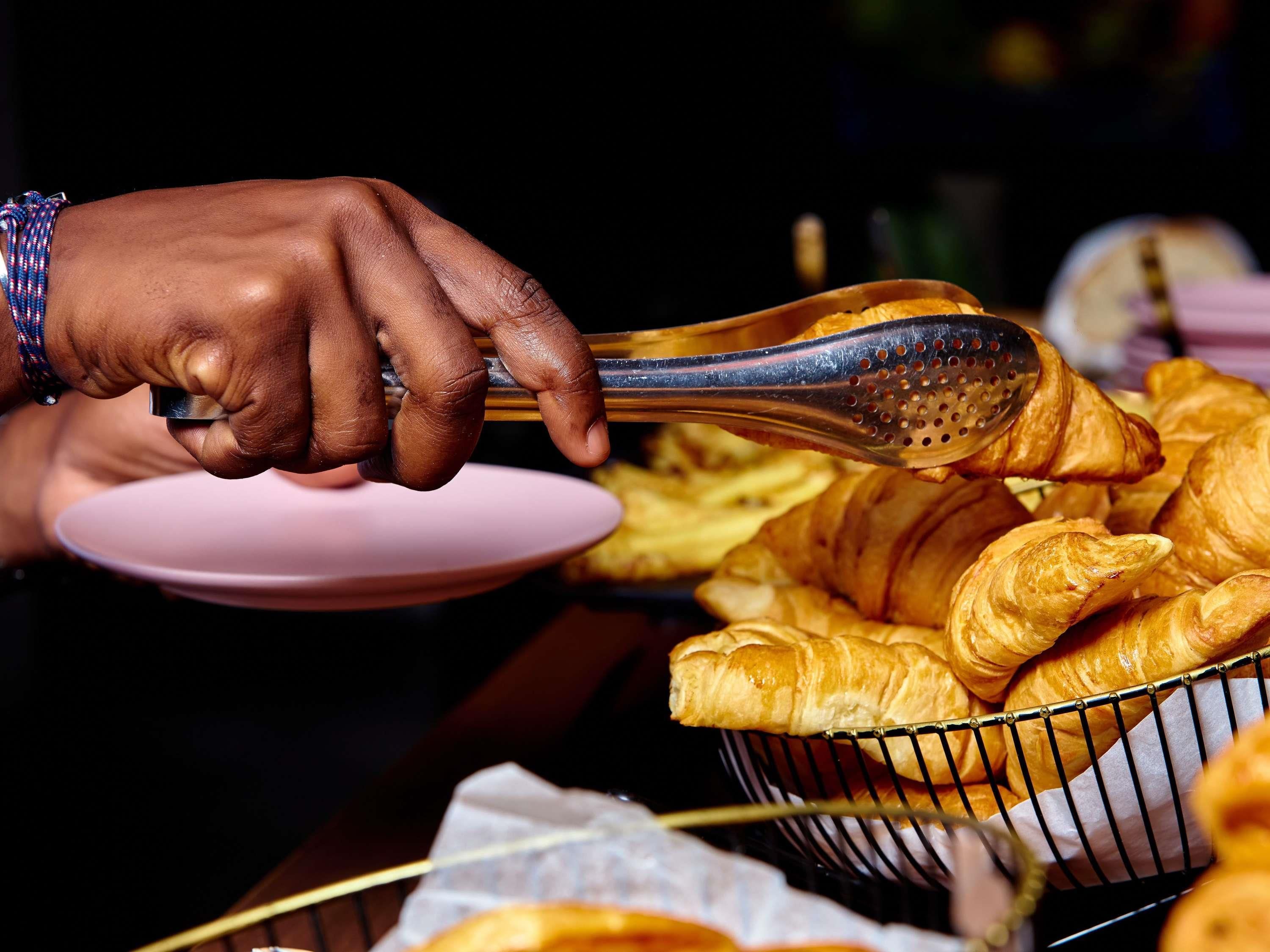 A person's hand holding tongs over a basket of croissants.