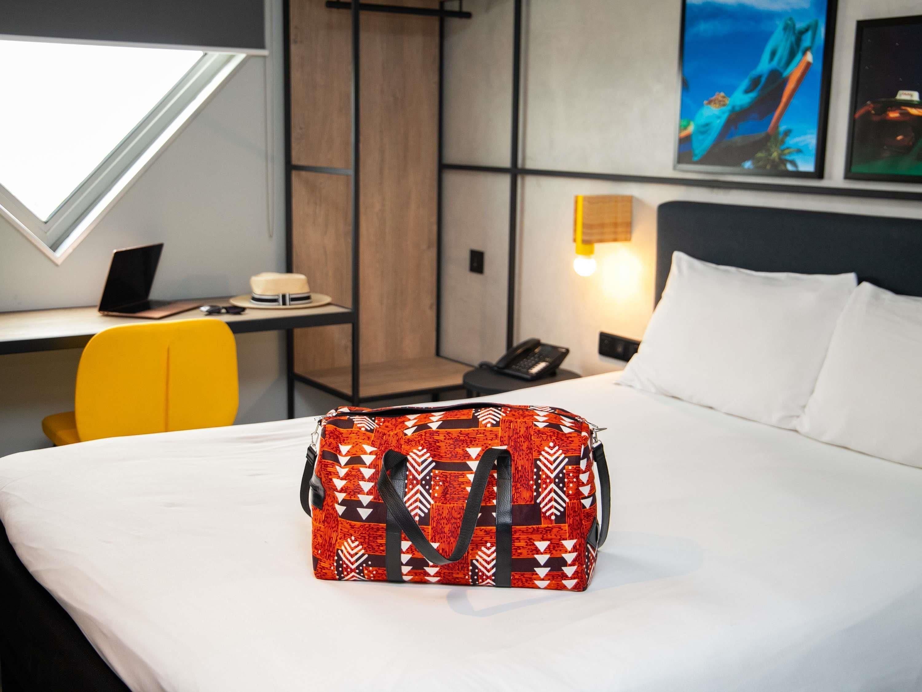 A hotel room with a bed, a desk with a laptop, a chair, and a bag on the bed.