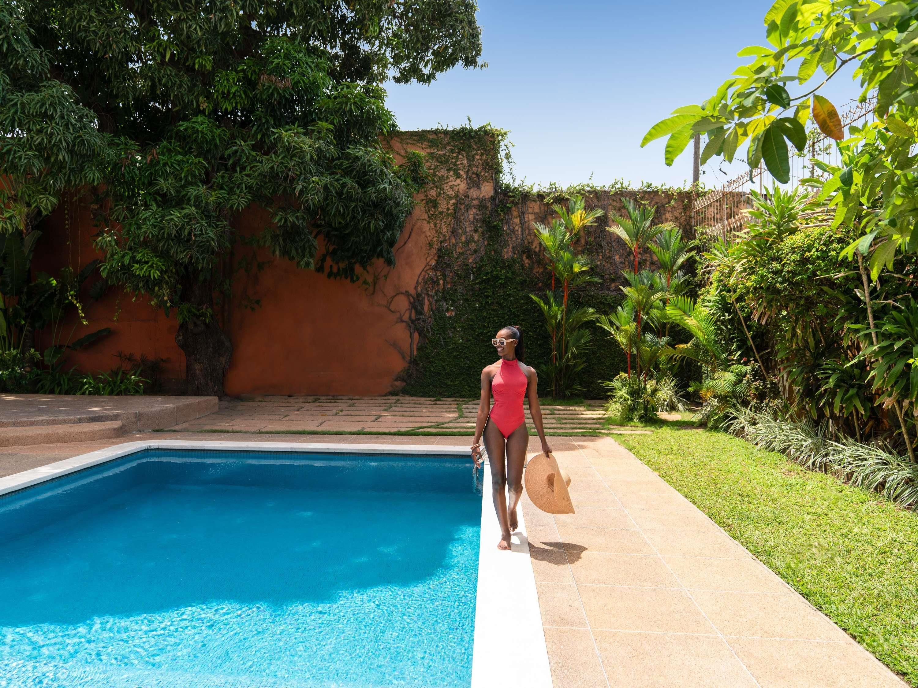 A swimming pool with a clear blue water surface, surrounded by lush greenery and a stone wall.