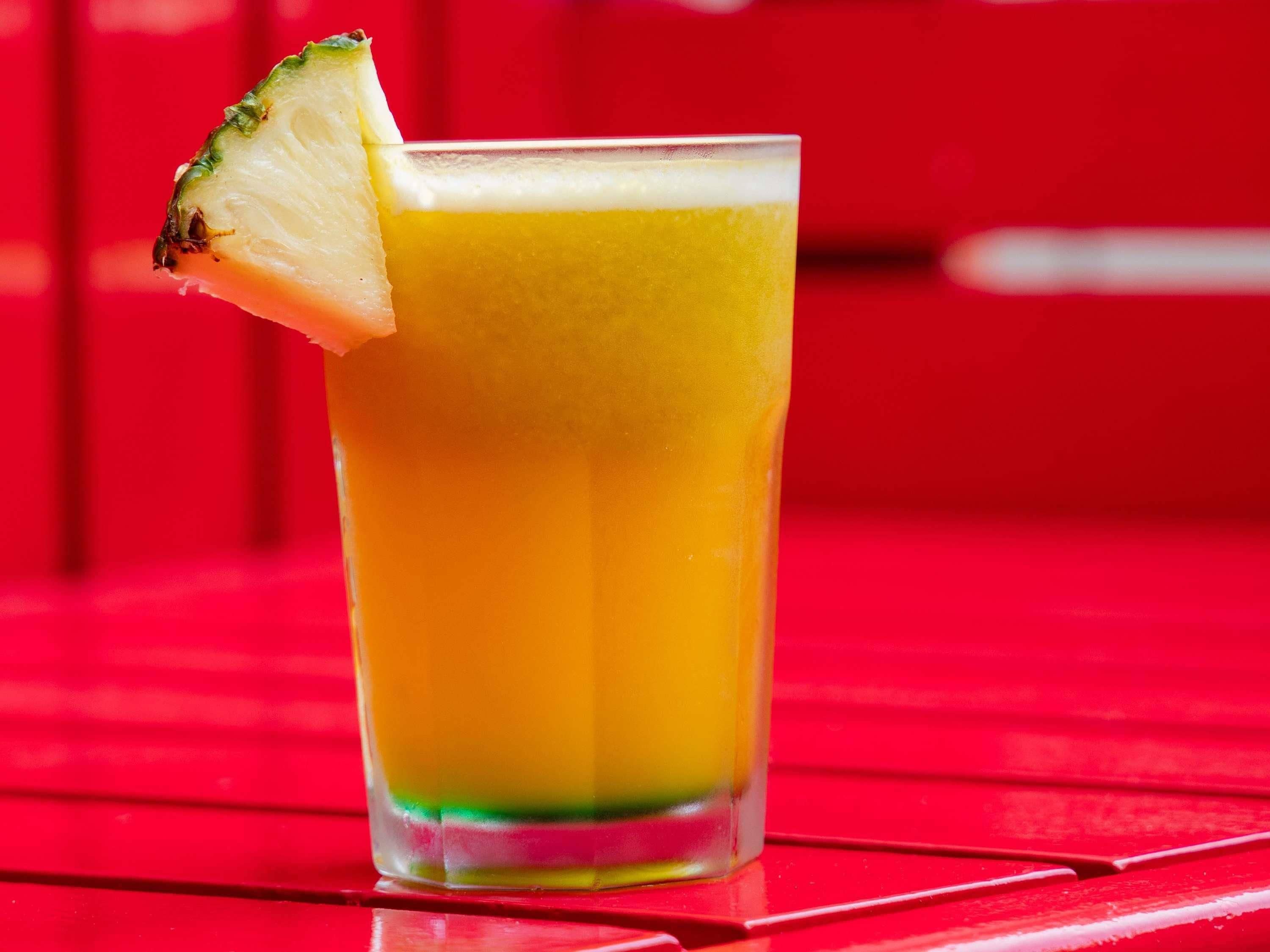 A tall glass of orange juice with a slice of lime on the rim, placed on a red surface.