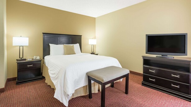 Quarto de hotel com uma cama, mesas de cabeceira, uma televisão e um banco.