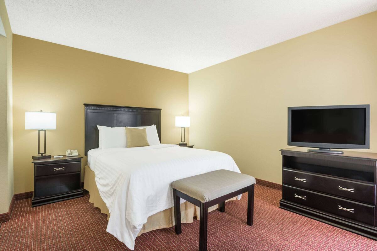 Una habitación de hotel con cama, mesitas de noche, televisor y un banco.