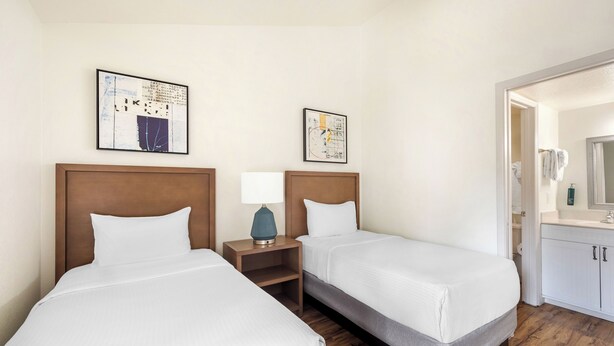 A hotel room with two beds, a wooden headboard, a nightstand with a lamp, and a bathroom visible through an open door. - Bryan’s Spanish Cove by Coolvacay (Orlando)