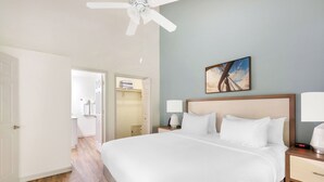 A hotel room with a large bed, a ceiling fan, a nightstand with a lamp, and a painting on the wall.