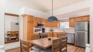 A modern kitchen with wooden cabinets, stainless steel appliances, and a dining area with a table and chairs.