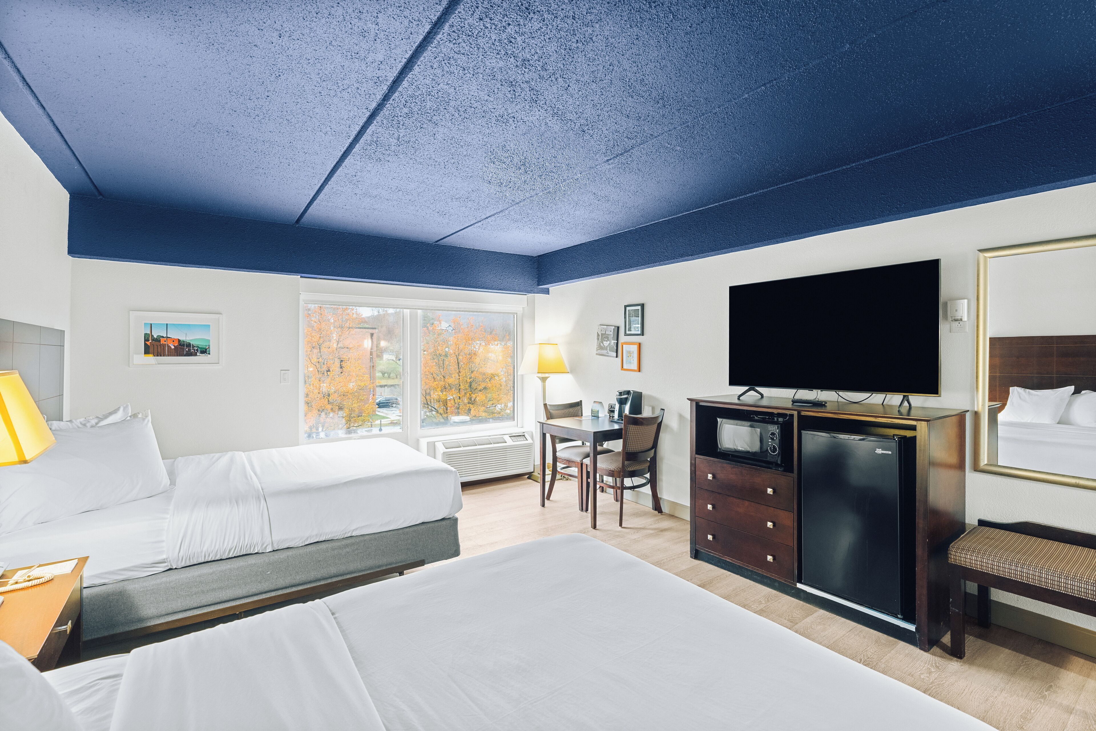 Quarto de hotel com duas camas, uma escrivaninha, televisão e cômoda.
