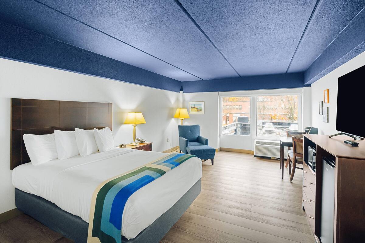 A hotel room with a large bed, a desk, a chair, and a view of the outside.