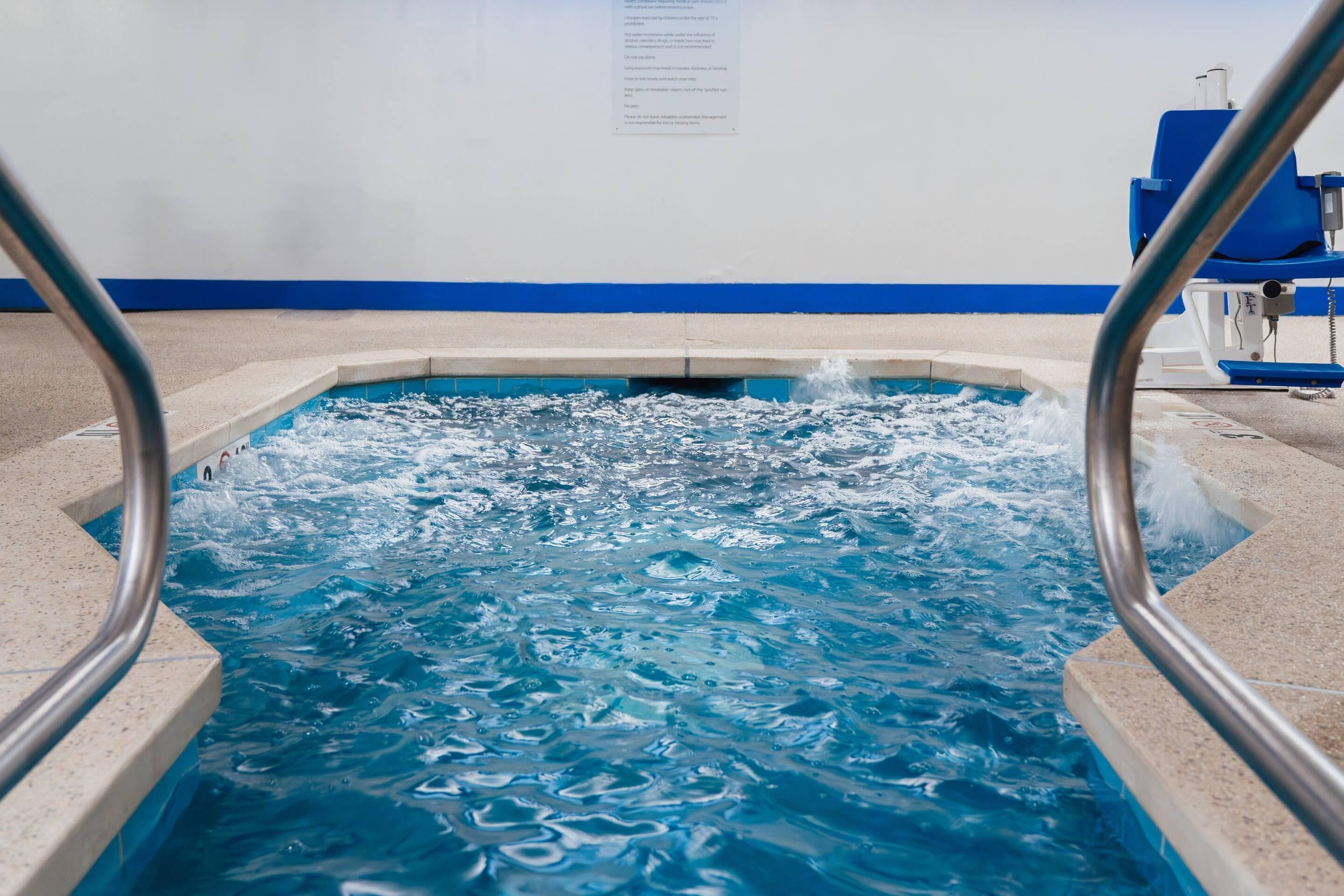 A swimming pool with clear water, a blue and white wall, and a metal pool ladder.