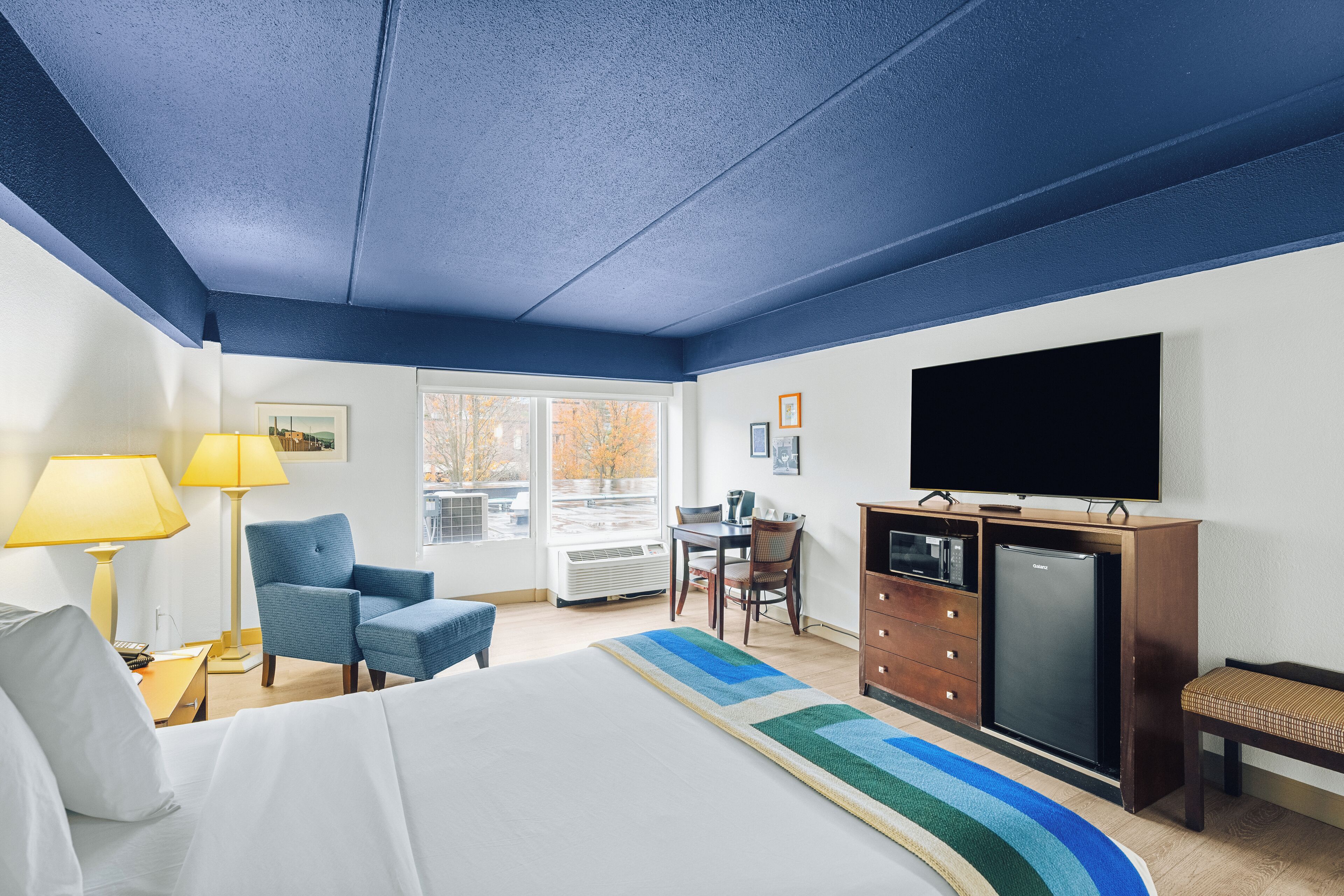 A hotel room with a bed, a desk, a chair, a television, and a refrigerator.