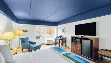 A hotel room with a bed, a desk, a chair, a television, and a refrigerator.