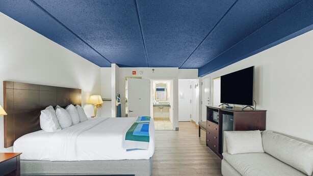 A hotel room with a bed, a sofa, a TV, and a bathroom visible through an open door.