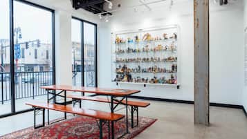 Una habitación con amplios ventanales, un tapete rojo con diseño, una mesa de madera con bancos y estanterías con figuritas.