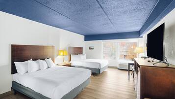 A hotel room with two beds, a desk, a TV, and a window with a city view.