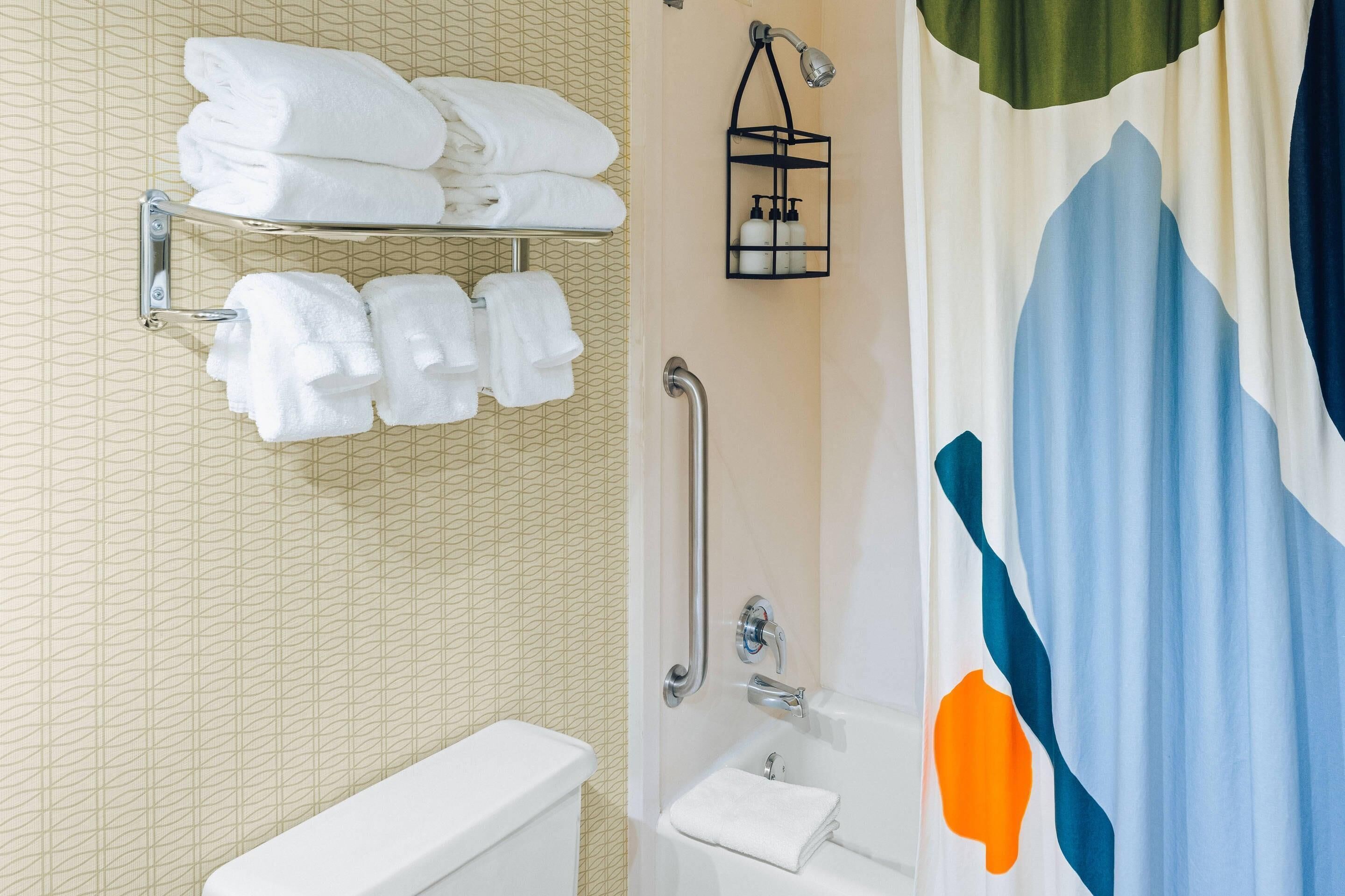 A bathroom with a toilet, a sink, a shower with a grab bar, and a towel rack with folded towels.