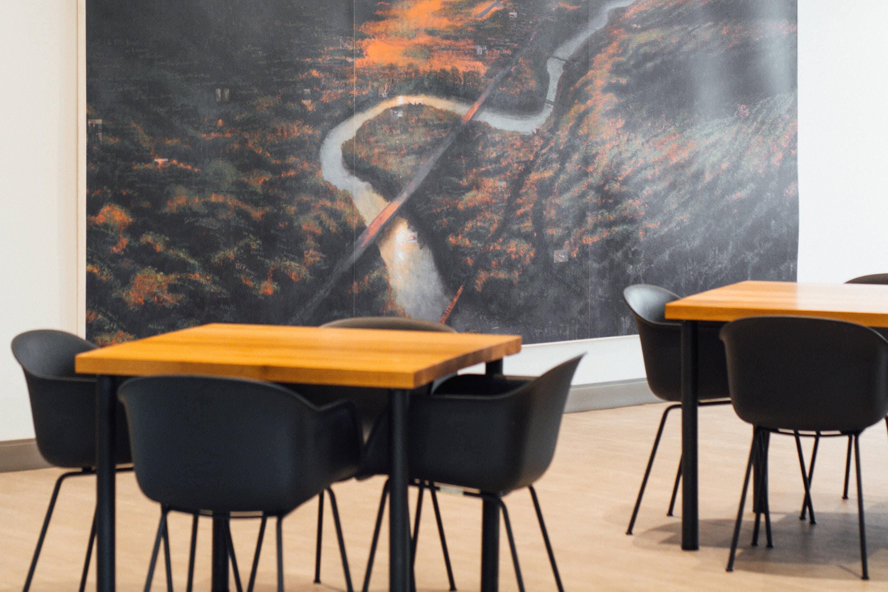 A modern dining area with wooden tables and black chairs, featuring a large abstract painting on the wall.