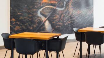 A modern dining area with wooden tables and black chairs, featuring a large abstract painting on the wall.