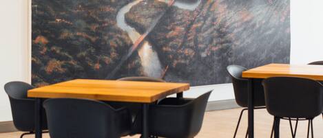 Un comedor moderno con mesas de madera y sillas negras, con un cuadro abstracto grande en la pared.