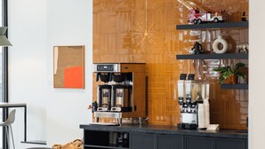 A modern cafe with a wooden accent wall, a coffee machine, and black chairs.