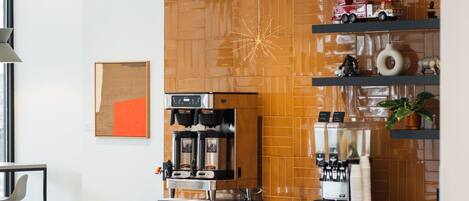 Una cafetería moderna con una pared decorada con madera, una máquina de café y sillas negras.