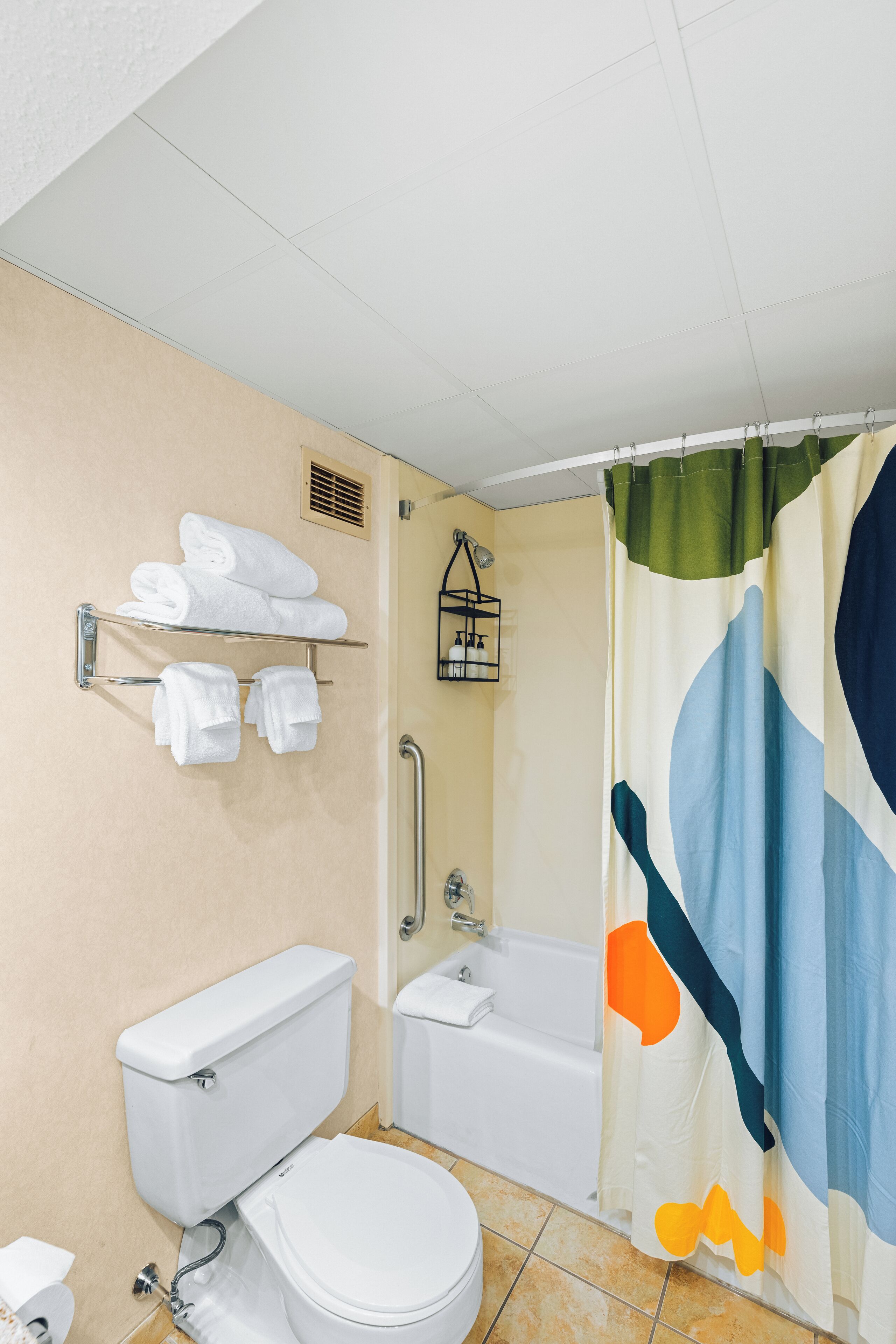 A bathroom with a toilet, a bathtub, and a shower curtain. There are towels on a rack and a small shelf with toiletries.