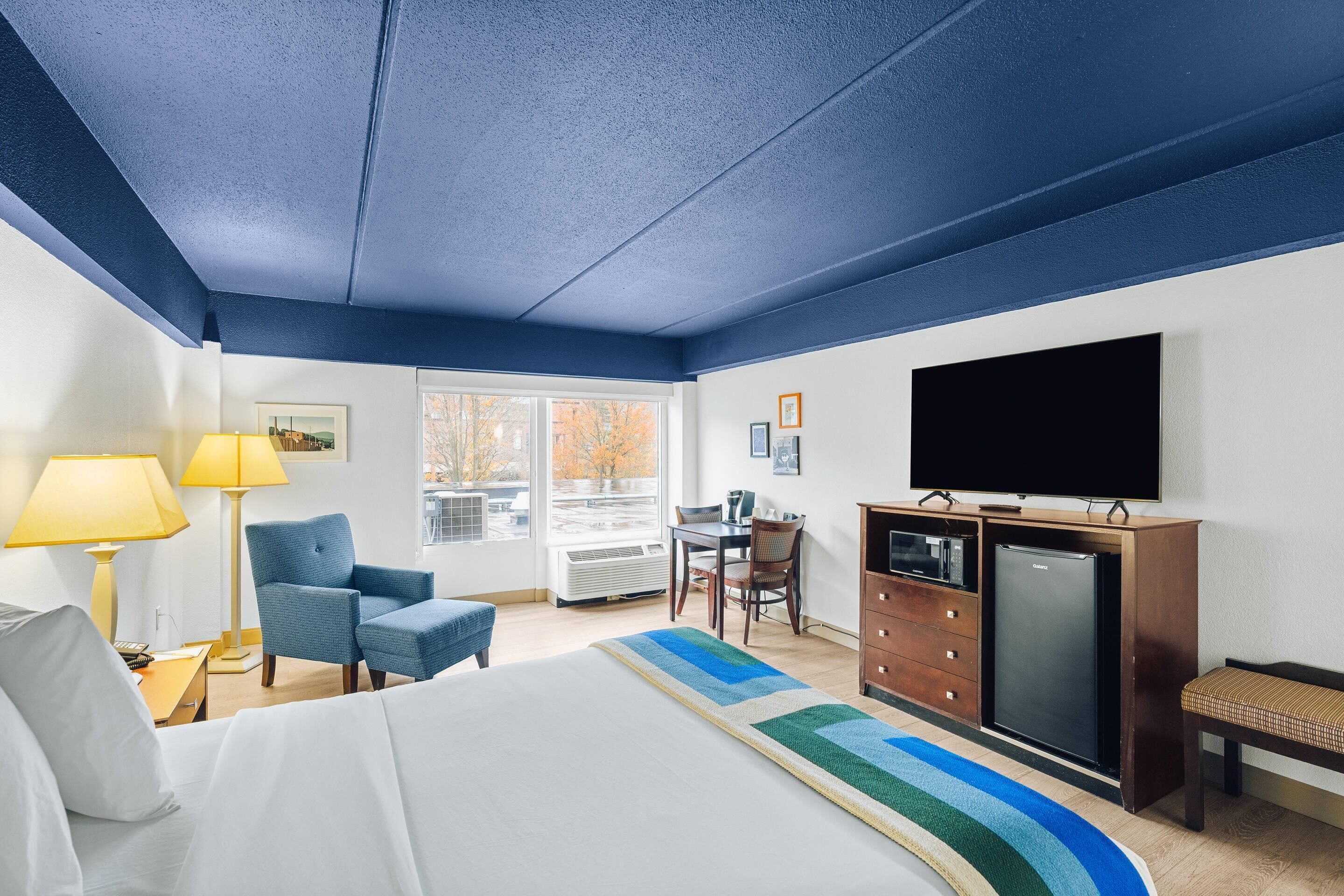 Una habitación de hotel con cama, escritorio, silla, televisor y cómoda.