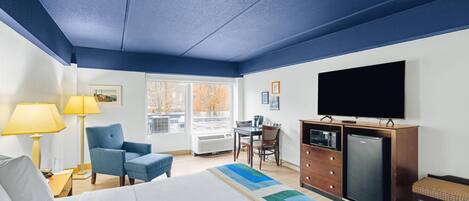 A hotel room with a bed, a desk, a chair, a television, and a dresser.