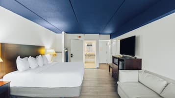 Habitació d'hotel amb un llit gran, un sofà, una televisió i un bany visible a través d'una porta oberta.