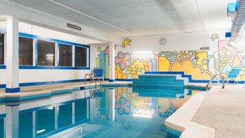 Una piscina interna con murales colorati sulle pareti, acqua cristallina e un’area solarium piastrellata.