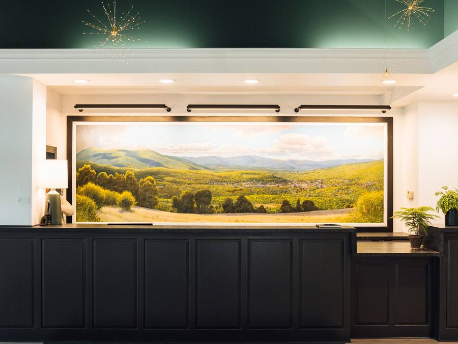 A reception area with a large landscape painting, a dark reception desk, and a potted plant.