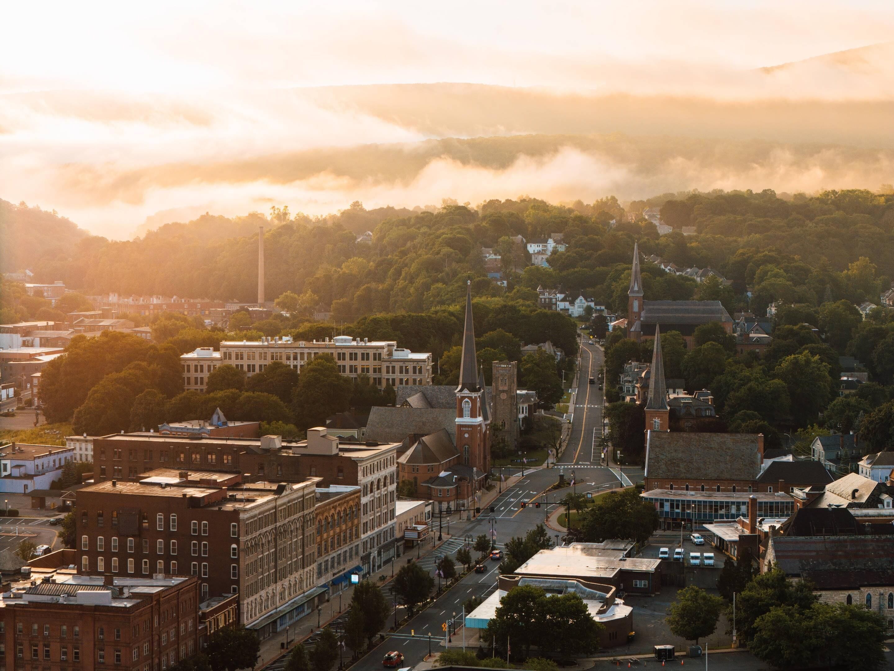 A cityscape with a prominent church steeple, a large building with a flat roof, and a road leading up a hill.