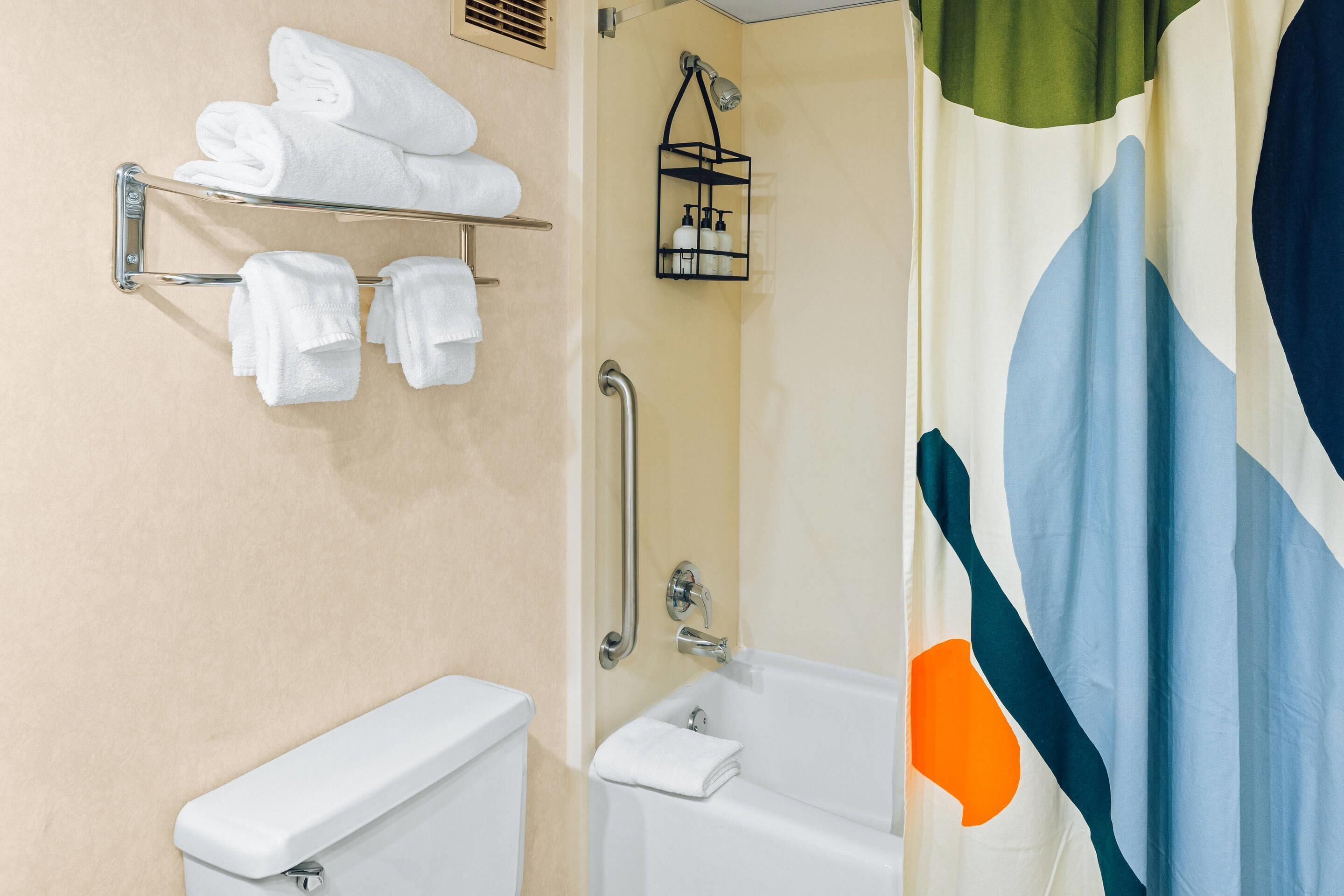 Un baño con inodoro, bañera, toallero con toallas dobladas y cortina de ducha.