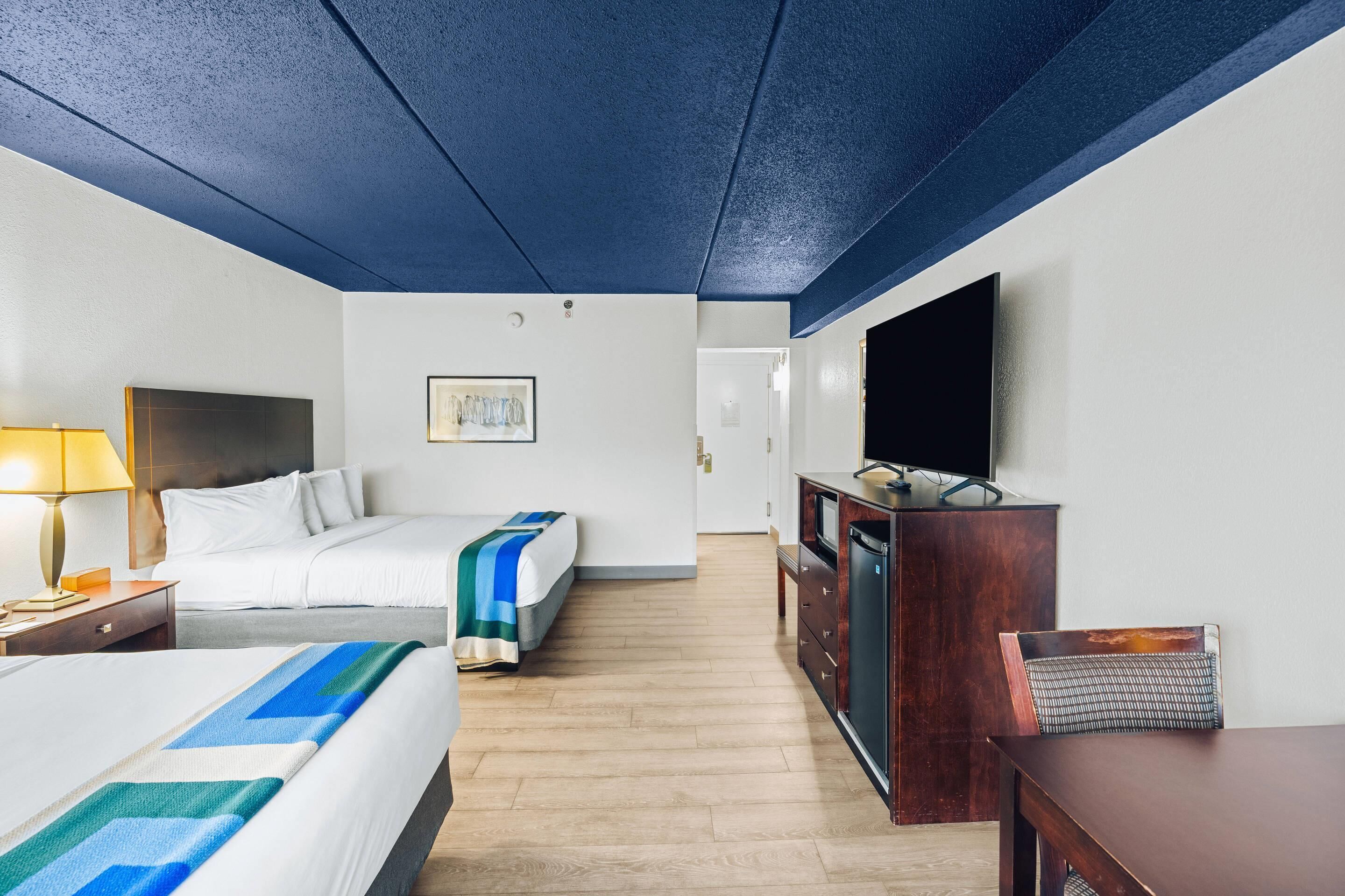 A hotel room with two beds, a TV, a wooden dresser, and a desk.