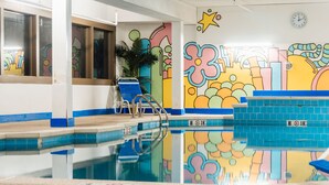 An indoor swimming pool with blue tiles, a clock on the wall, and colorful graffiti art.